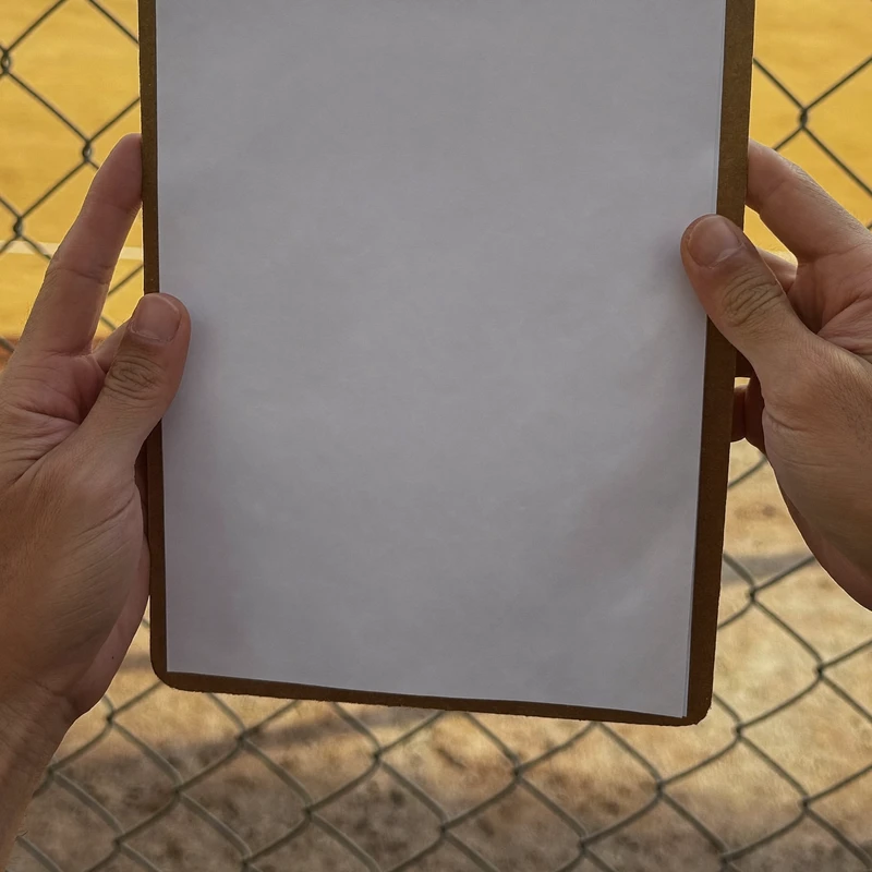 Hands holding a clipboard at a ballfield fence