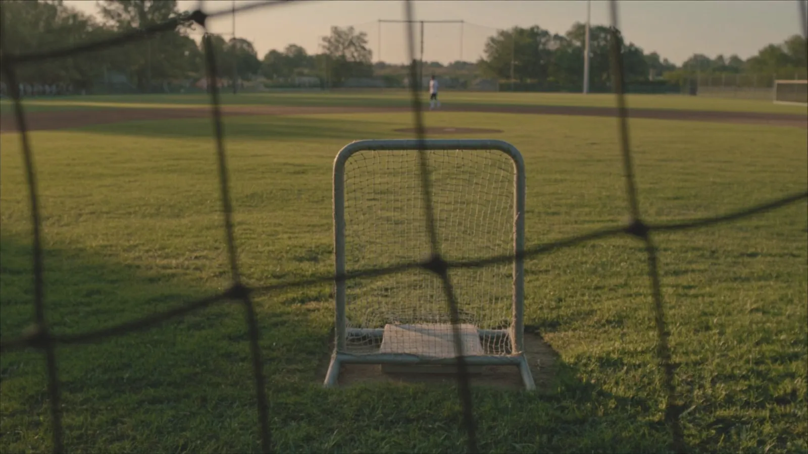 An empty baseball diamond at golden hour seen through the backstop netting
