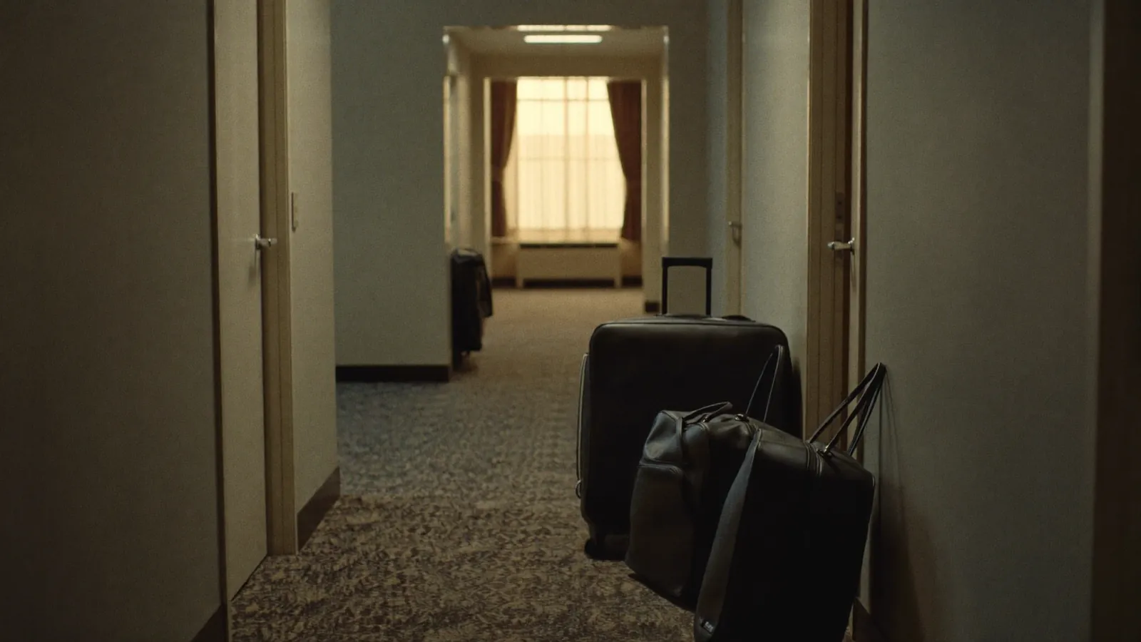Black duffel bags standing against the wall of a quiet hotel corridor at dawn