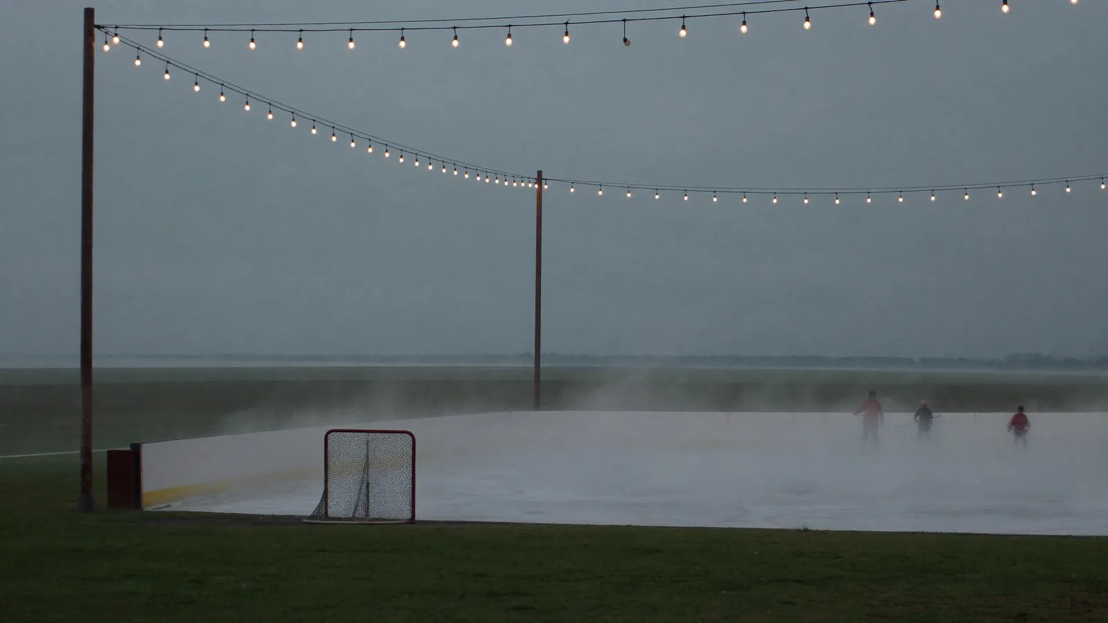 An outdoor hockey rink at dusk under strings of lights, mist over the ice and tiny skaters in the distance