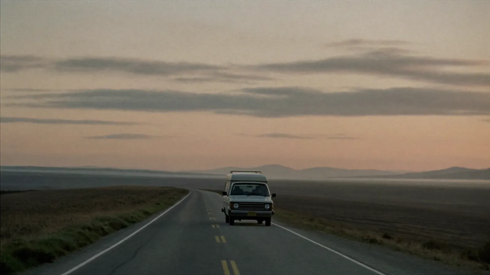 A minivan driving a long country road at sunrise